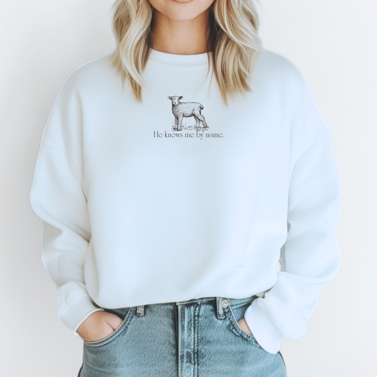 White Christian sweatshirt with lamb graphic and text "He Knows Me By Name" inspired by John 10. 