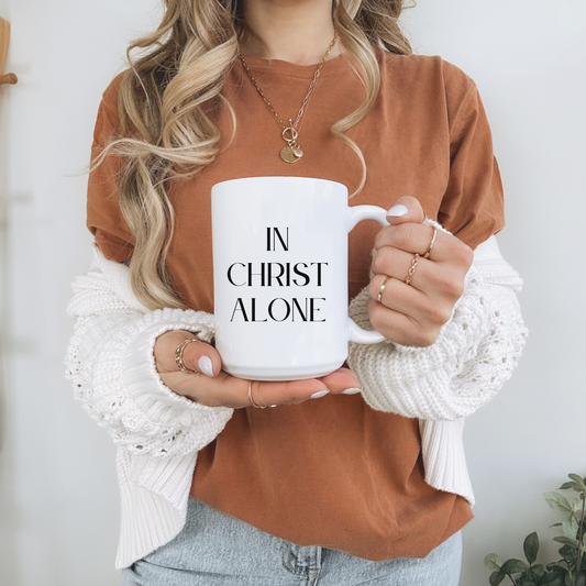 Large 15oz white Christian mug with bold black text reading "In Christ Alone". Scripture-inspired coffee mug for daily use. 