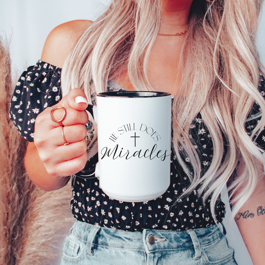 Christian ceramic mug with black interior and handle featuring cross design and text that says "He Still Does Miracles."