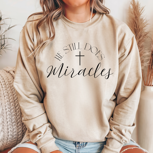 Christian sweatshirt in sand color with black text. Inspirational text in black saying "He still does miracles" with cross. 