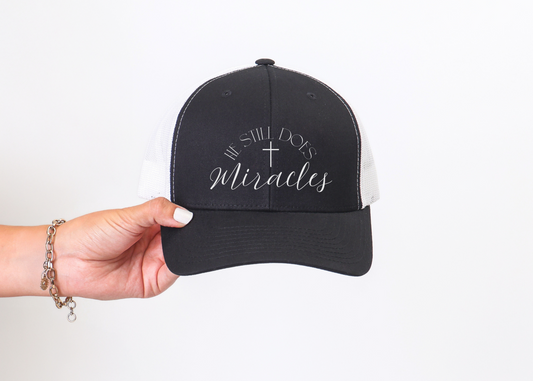 Christian trucker hat with embroidered cross and text "He still does miracles".