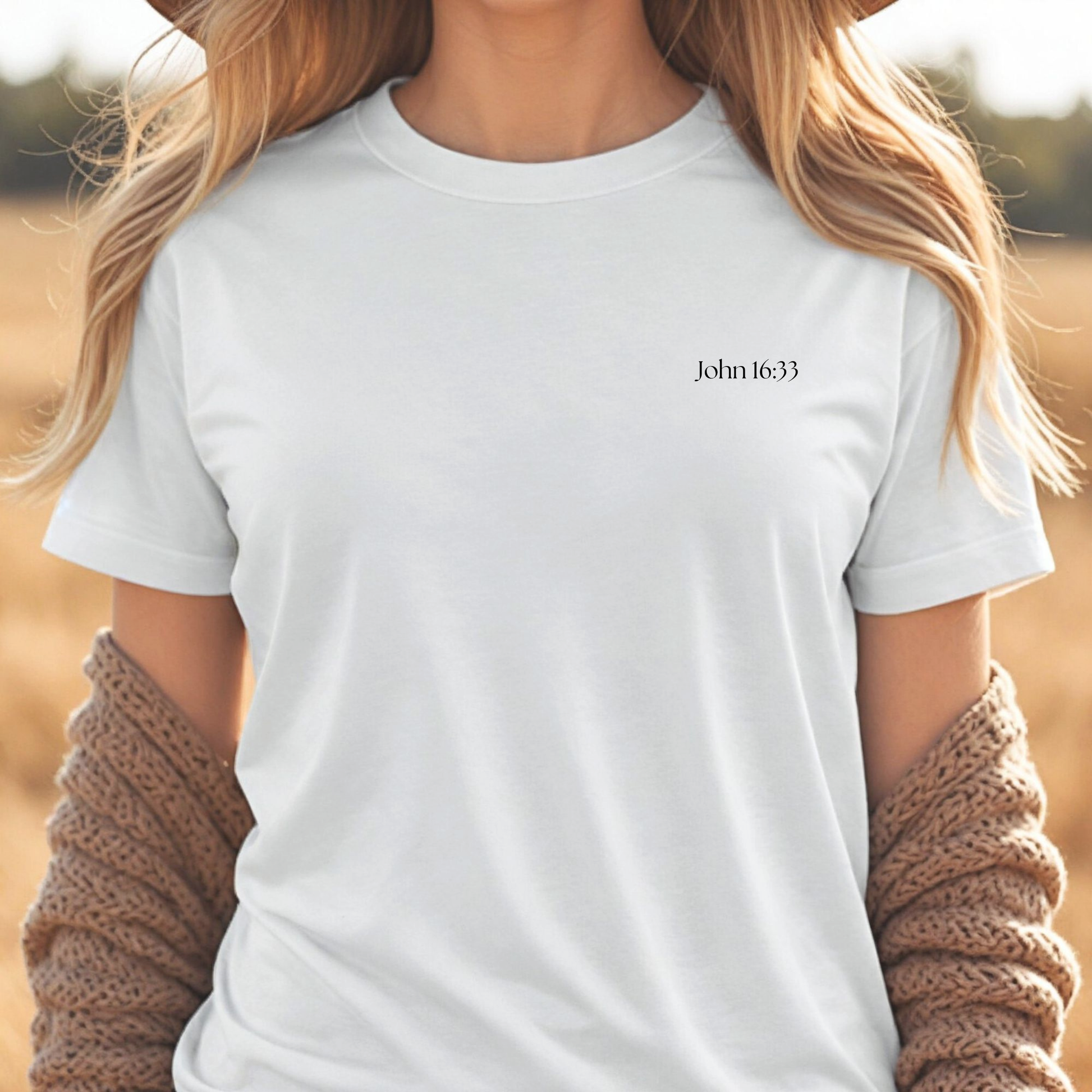 Person wearing a white christian t-shirt with 'John 16:33' text in a natural setting.